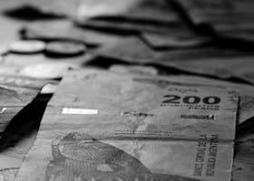 Home Black and white photo of Argentine peso banknotes and coins in Buenos Aires.