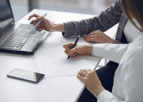 Home Two professionals collaborating on business plans using a laptop and paper documents.